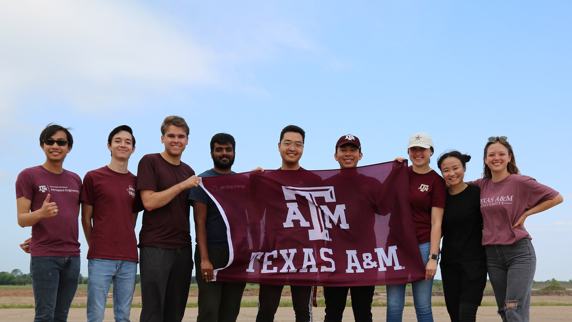 Students smiling for a photo while holding a Texas A&M University flag.