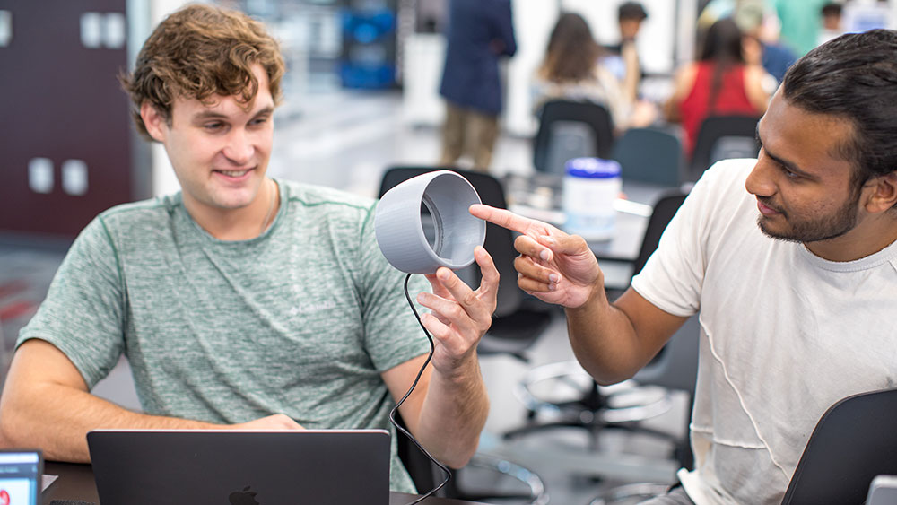 Two male students looking at medical device in Engineering Medicine classroom.