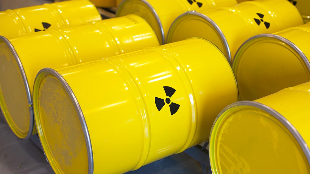 rows of yellow metal barrels with the symbol for hazardous waste on them