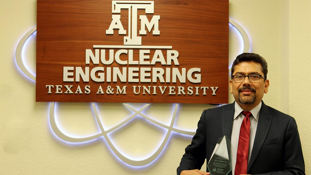 Sunil Chirayath stands next to the Nuclear Engineering sign while holding his award.